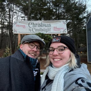 A young couple stands for a photo by a banner that says Welcome to Christmas by Candlelight