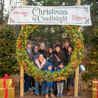 A family of adults and kids take a photo together with a giant Christmas wreath