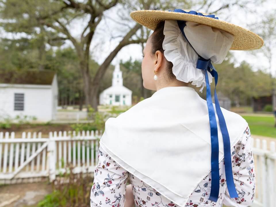 Back view of a lady oin colonial dress including a cap and straw hat