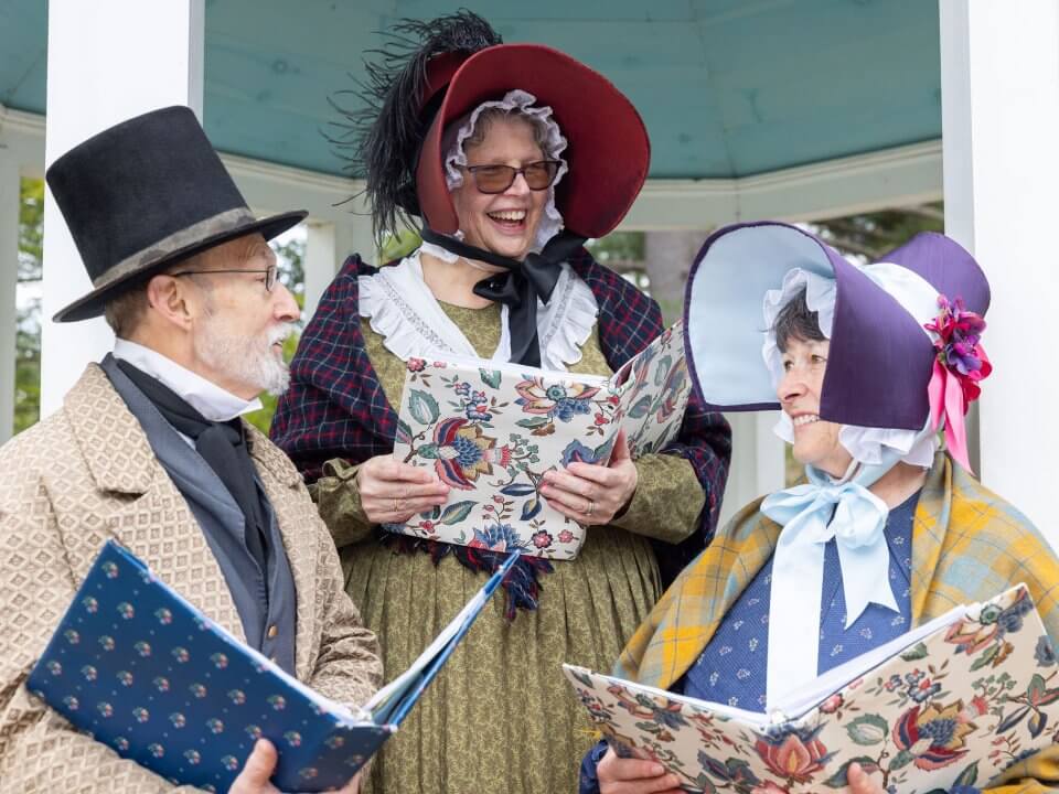 Three adults wearing 1830s style clothing and holding colorful bound books