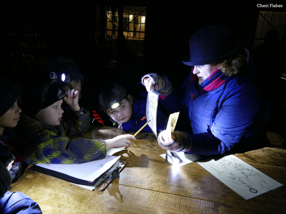 Kids look at documents and clues with an adult educator at night with flashlights and headlamps